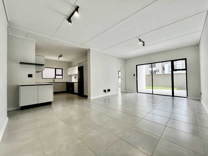 Modern open-plan living area featuring neutral tiled flooring, sleek kitchen cabinetry, and large sliding glass doors leading to an outdoor space.