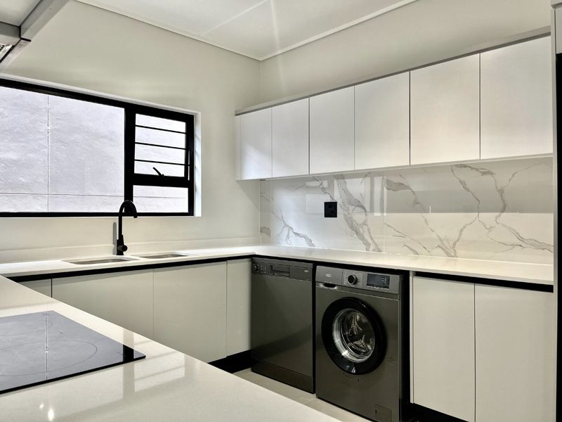 Modern kitchen featuring sleek white cabinetry, stone countertops, marble-look splashback, and integrated appliances including a dishwasher and washing machine.