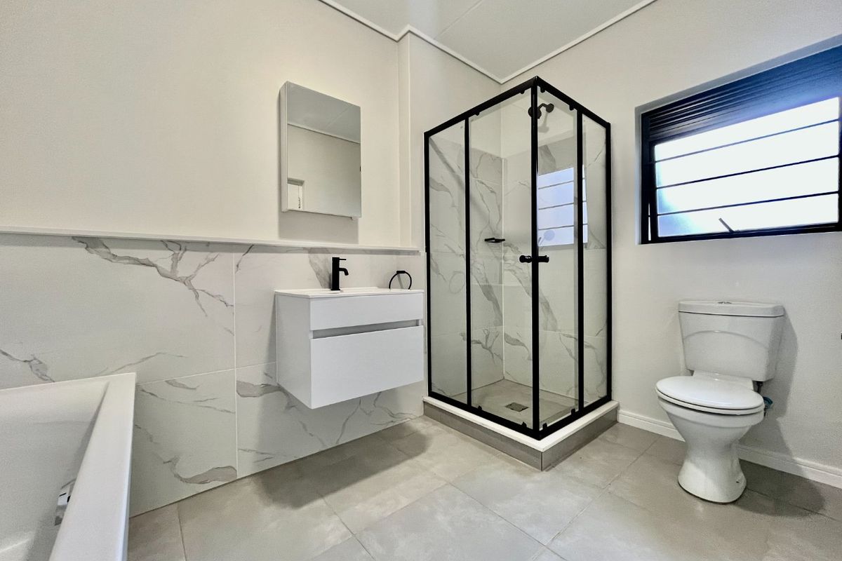 Modern bathroom featuring a floating vanity, black-framed shower enclosure, marble-look wall tiling, and a clean, contemporary aesthetic.
