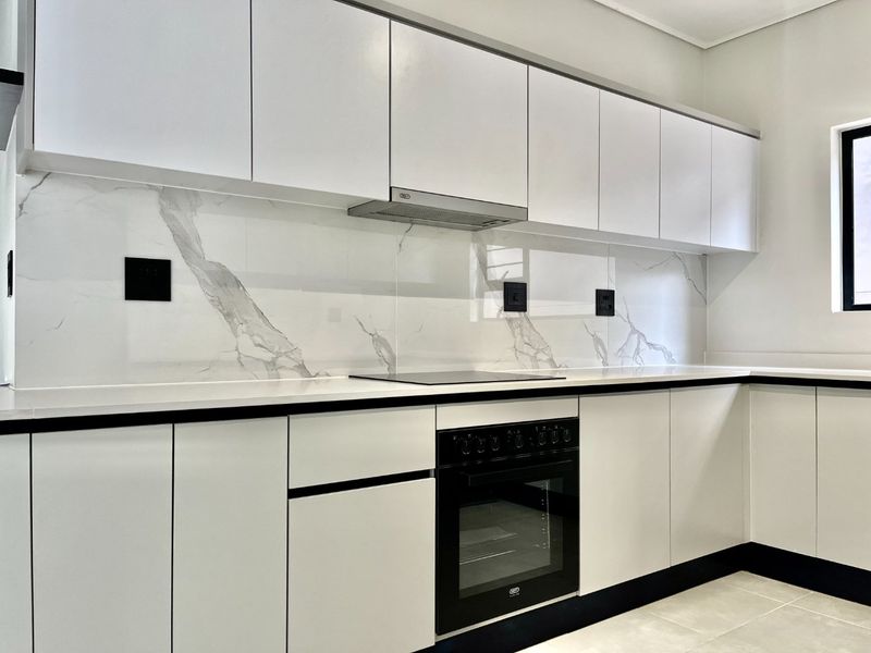 Modern kitchen featuring sleek white cabinetry, marble-look splashback, integrated electric hob, built-in oven, and high-quality stone countertops.