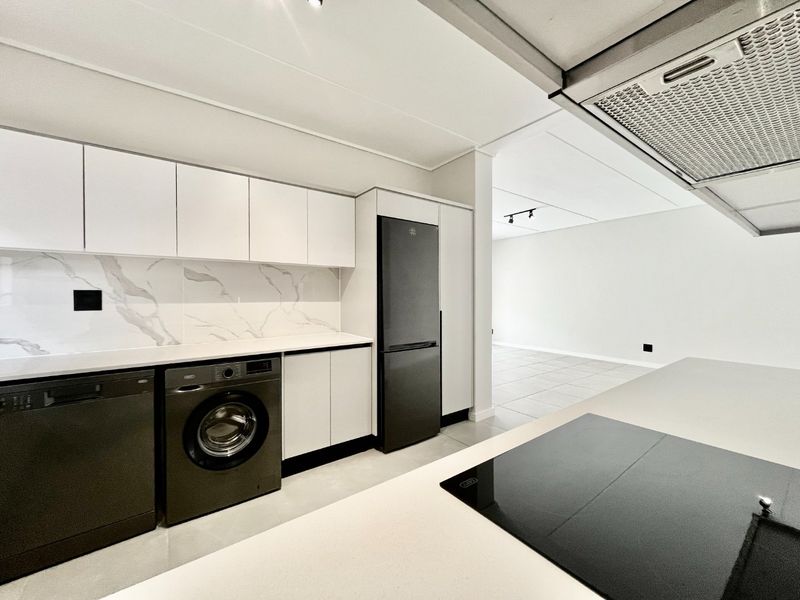 Modern kitchen featuring sleek white cabinetry, marble-look splashback, stone countertops, and integrated appliances, flowing into an open-plan living area.