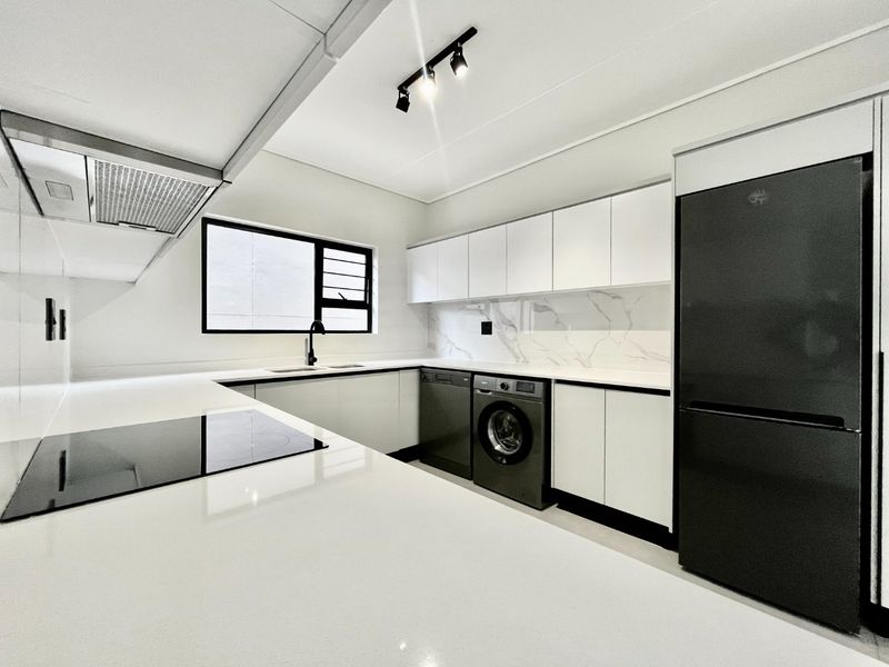 Modern kitchen featuring sleek white cabinetry, stone countertops, marble-look splashback, integrated appliances, and contemporary track lighting.