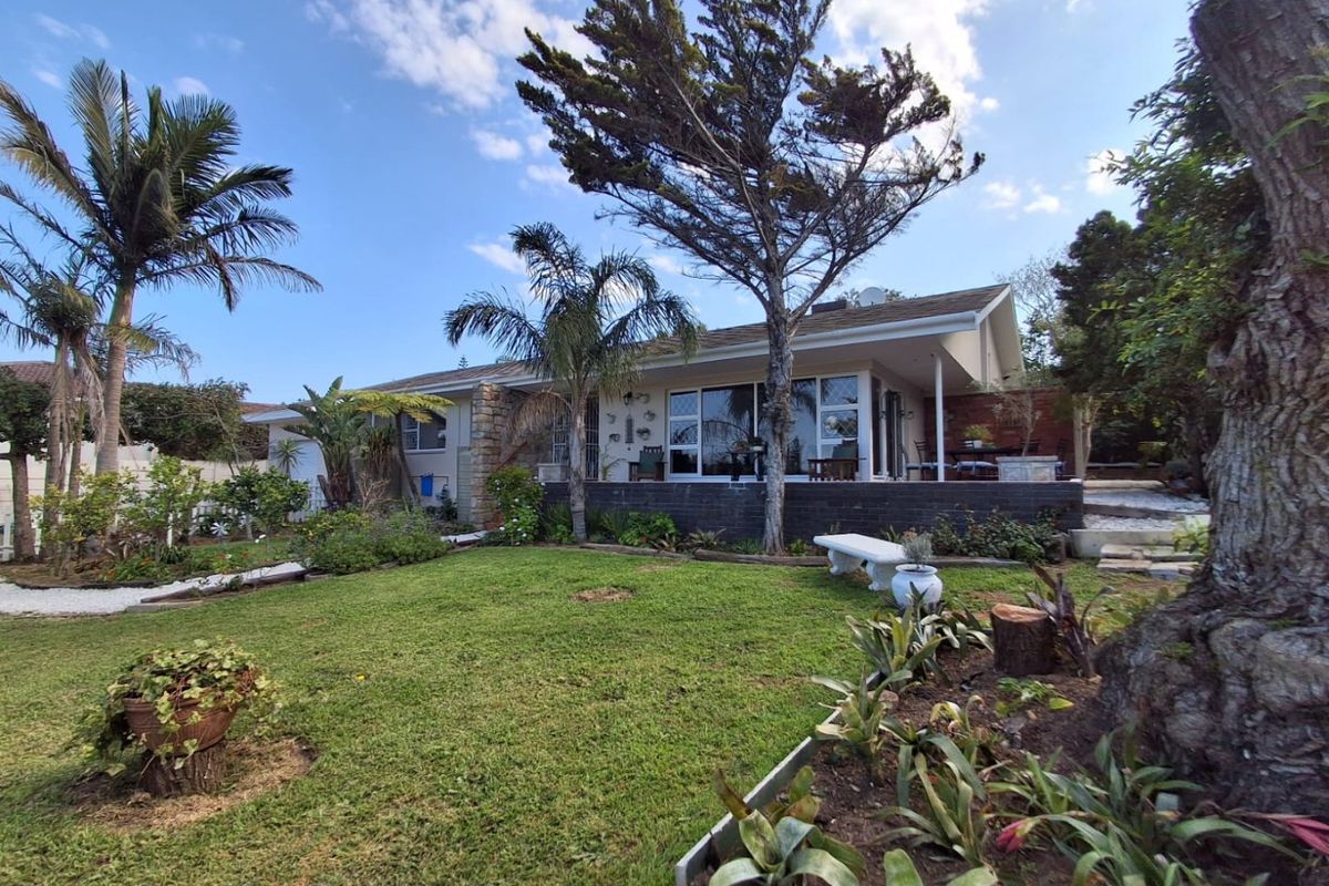 Rear view of the house featuring a covered patio, sliding glass doors, and a well-maintained garden with mature trees.