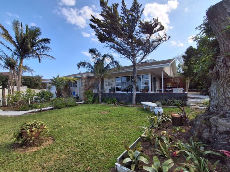 Rear view of the house featuring a covered patio, sliding glass doors, and a well-maintained garden with mature trees.