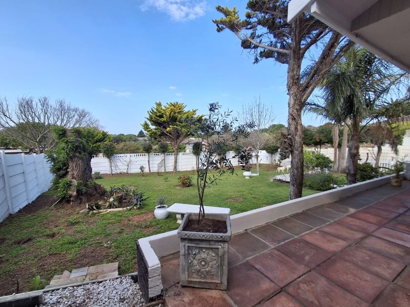 A spacious rear garden featuring a tiled patio area, mature trees, and a secure precast concrete boundary wall.