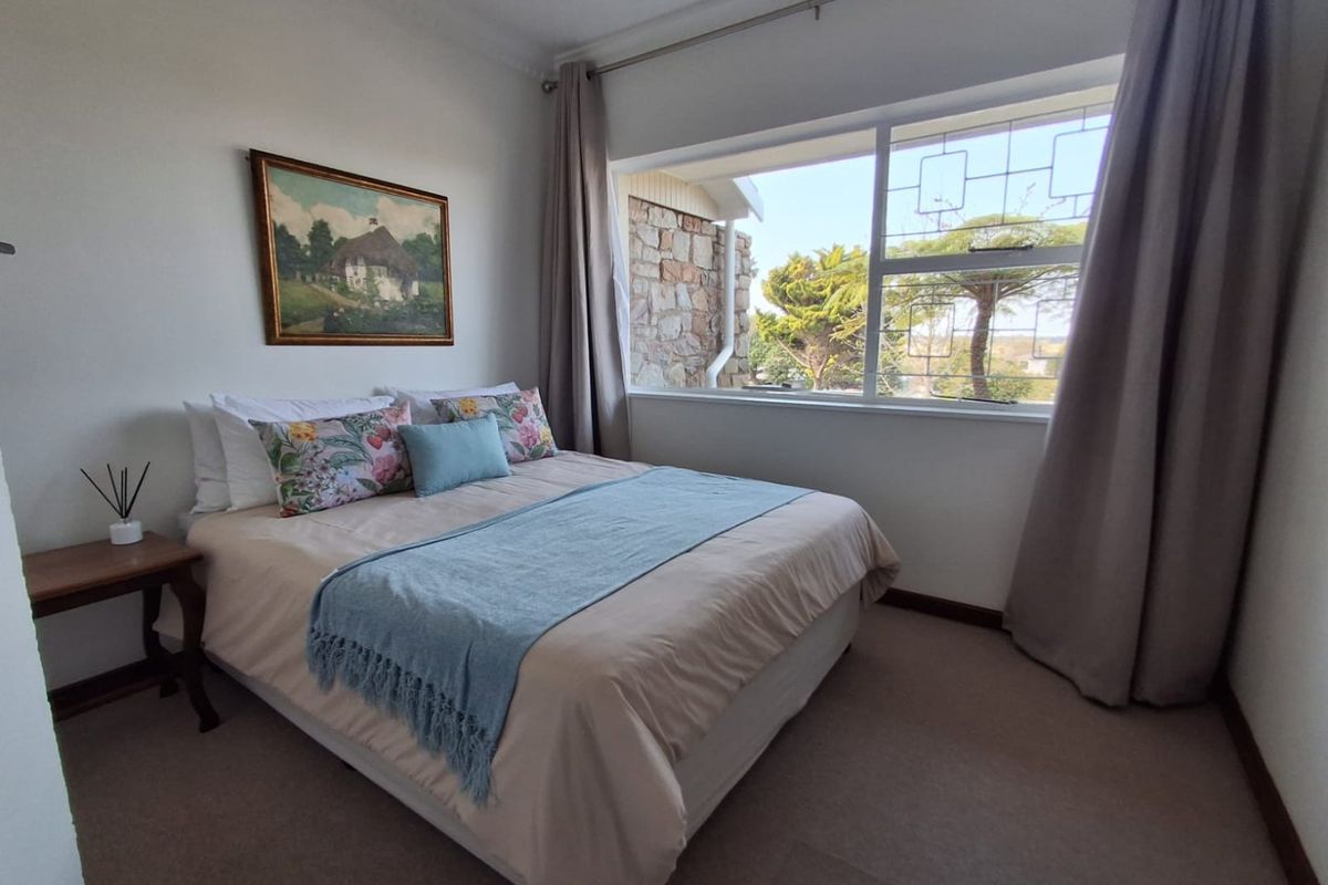A well-lit bedroom featuring neutral carpeting, a large window with garden views, and classic cornice detailing.