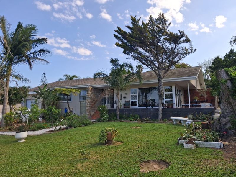 Rear view of the house featuring a landscaped garden, raised patio area, stone facade accents, and large sliding glass doors leading to the interior.
