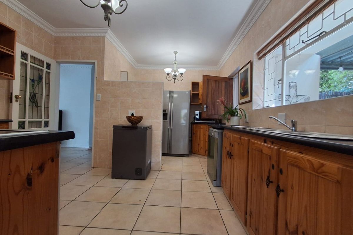 A functional kitchen featuring wooden cabinetry, tiled backsplash, and tiled flooring, illuminated by dual chandeliers with a classic coved ceiling finish.
