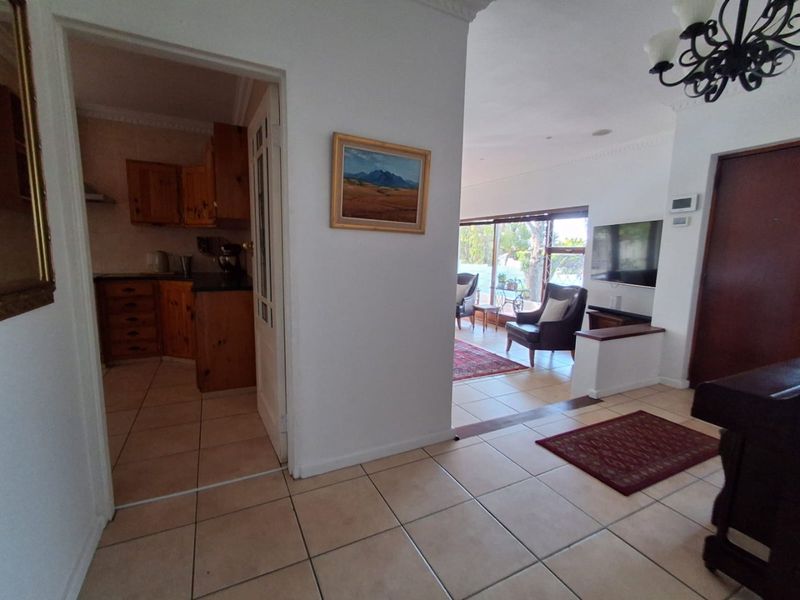 Open plan living area featuring tiled floors, cornicing, and a view through to the kitchen and rear patio area.