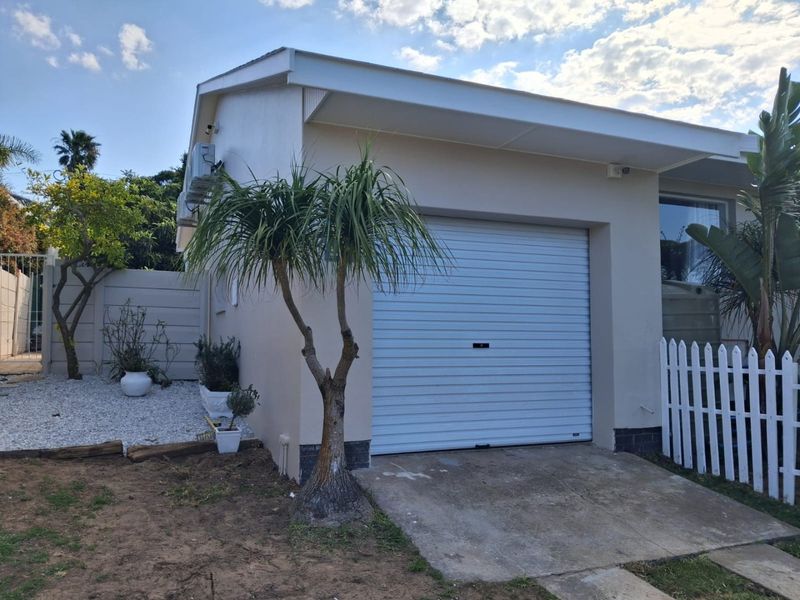 A well-maintained single garage featuring a roller shutter door, concrete driveway, and exterior air conditioning unit, set within a tidy garden area.