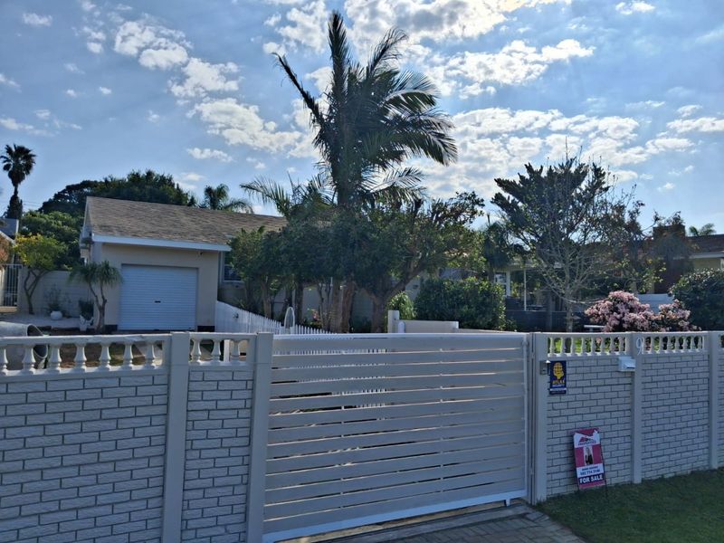 Front view of the property featuring a secure brick boundary wall, slatted metal gate, paved driveway, and a single garage.