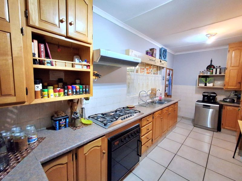 A functional kitchen featuring wooden cabinetry, a gas hob with extractor fan, built-in oven, double sink, and tiled flooring.