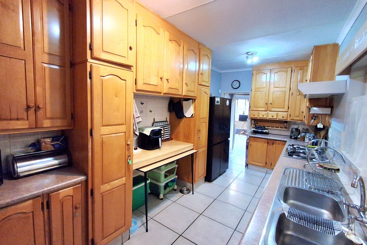 A functional kitchen featuring extensive wooden cabinetry, laminate countertops, a double stainless steel sink, and a gas hob with an extractor fan.