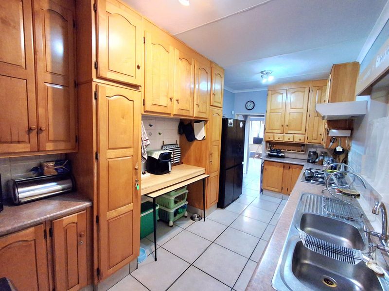 A functional kitchen featuring extensive wooden cabinetry, laminate countertops, a double stainless steel sink, and a gas hob with an extractor fan.