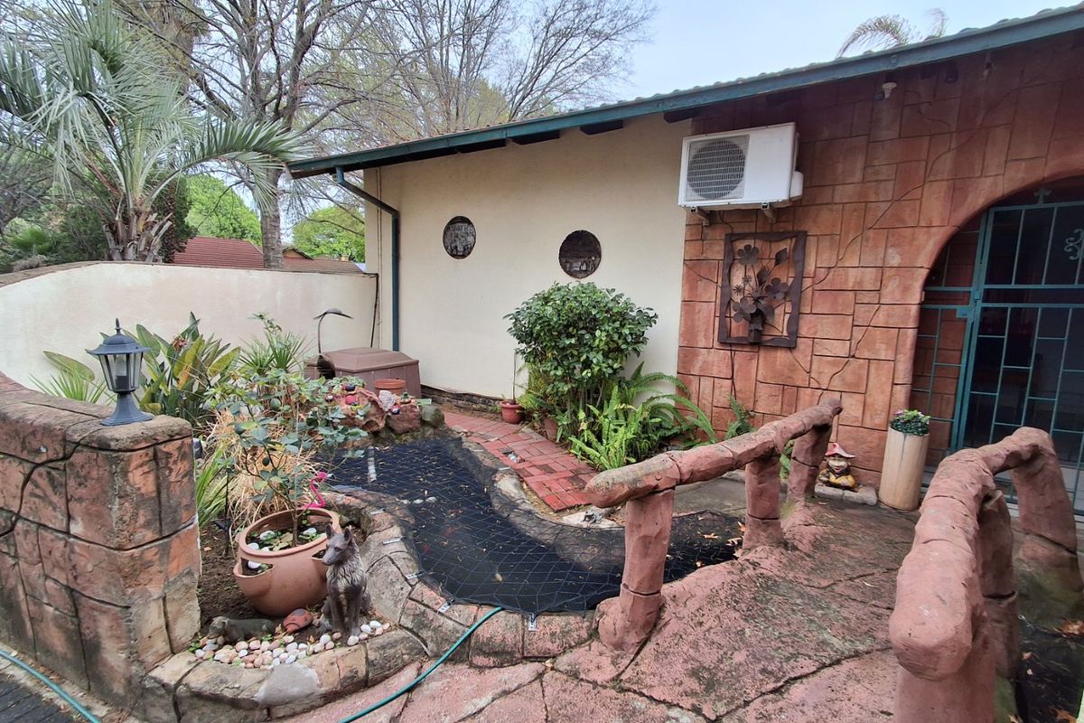 Rear garden area featuring a small pond, stone-clad bridge, paved patio, and exterior wall with a mounted air conditioning unit.