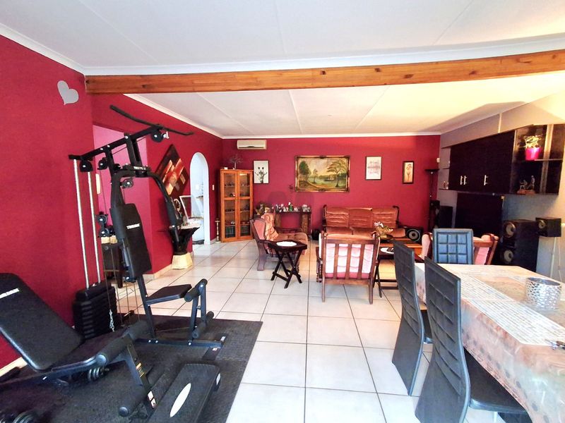 Spacious open-plan living and dining area featuring tiled flooring, an exposed timber ceiling beam, and a wall-mounted air conditioning unit.