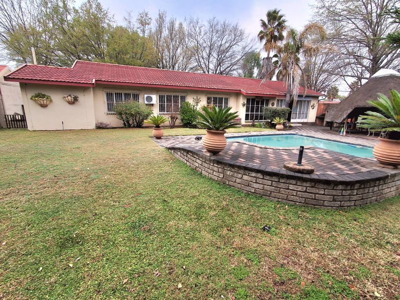 Rear view of the property featuring a swimming pool, brick paved surround, and a lawn area with a tiled roof house facade.