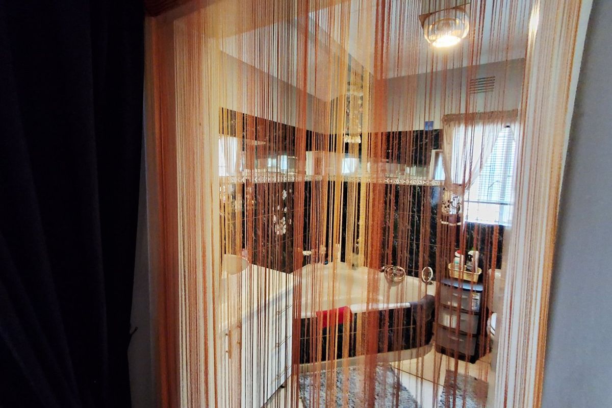 A bathroom featuring a corner bathtub, vanity cabinet, and tiled walls, viewed through a decorative string curtain.