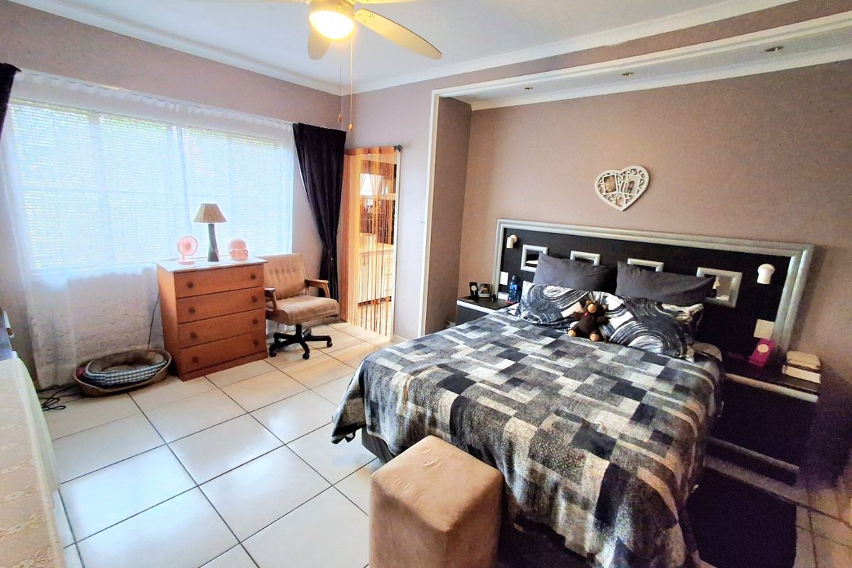 Spacious bedroom featuring tiled flooring, a built-in headboard with integrated lighting, and a ceiling fan.
