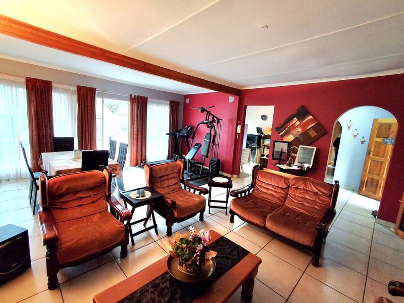 Spacious open-plan living and dining area featuring tiled flooring, an exposed timber ceiling beam, and direct access to the outdoors via sliding glass doors.