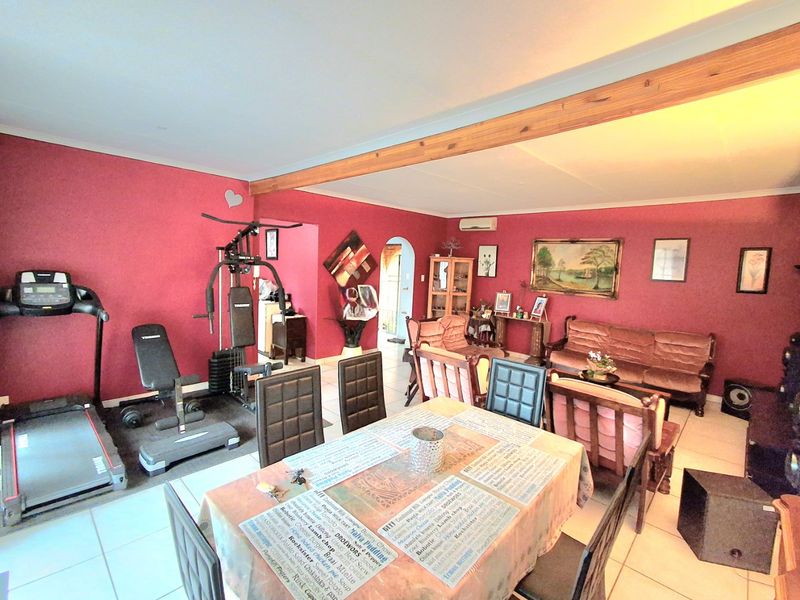 Spacious open-plan living and dining area featuring tiled flooring, an exposed timber ceiling beam, and a wall-mounted air conditioning unit.