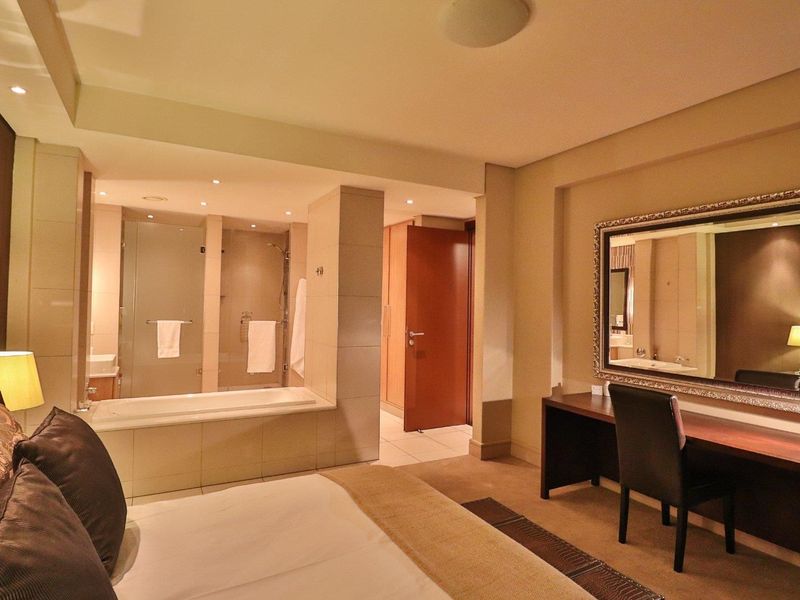 Spacious bedroom featuring an integrated en-suite bathroom with a built-in bathtub and glass shower enclosure, finished with neutral tiling and recessed lighting.