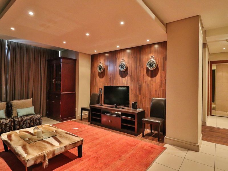 A well-maintained living room featuring a recessed ceiling with integrated downlights, wood veneer feature wall paneling, and neutral tiled flooring.