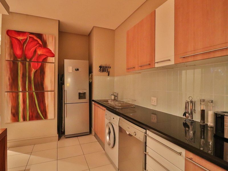 A functional kitchen featuring modern cabinetry, stone countertops, tiled backsplash, and integrated plumbing for appliances, finished with neutral floor tiles.