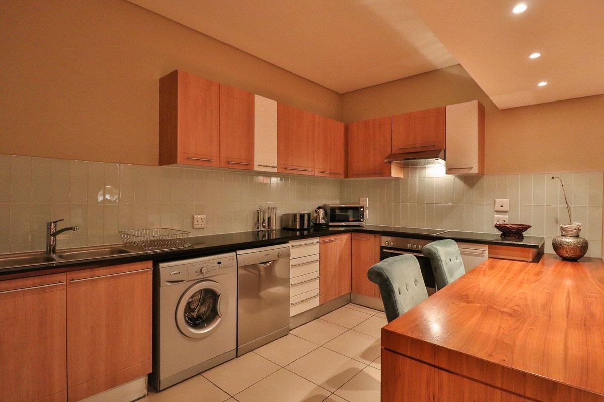A functional kitchen featuring wood-finish cabinetry, granite countertops, a tiled backsplash, and integrated appliances including an oven and extractor fan.