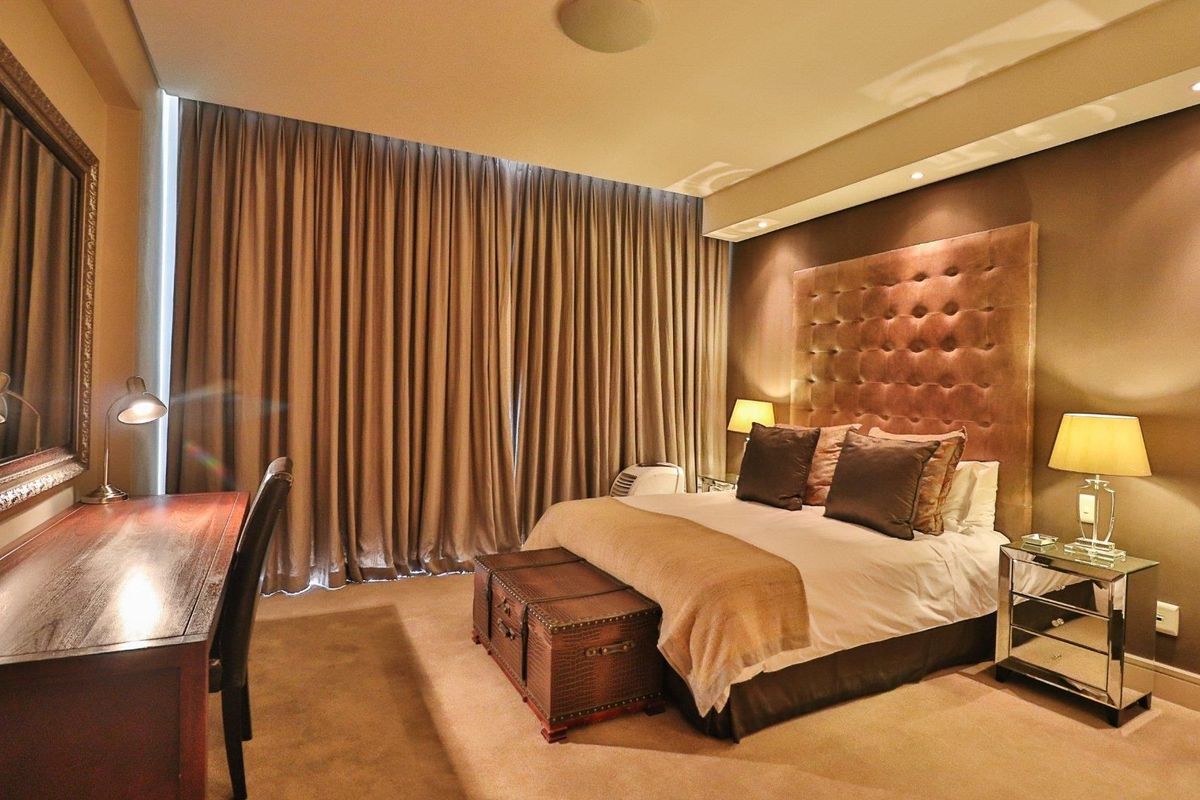 A well-appointed bedroom featuring plush carpeting, a large upholstered headboard, and full-length curtains providing a warm and comfortable atmosphere.