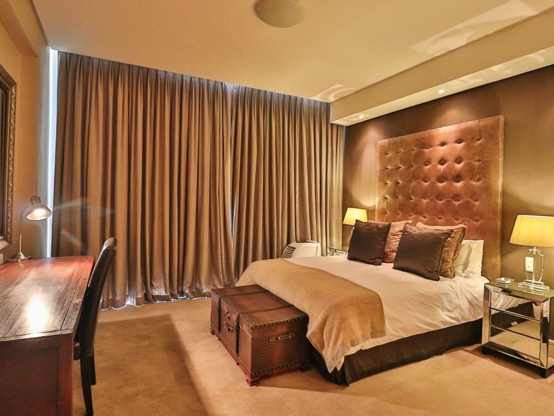 A well-appointed bedroom featuring plush carpeting, a large upholstered headboard, and full-length curtains providing a warm and comfortable atmosphere.