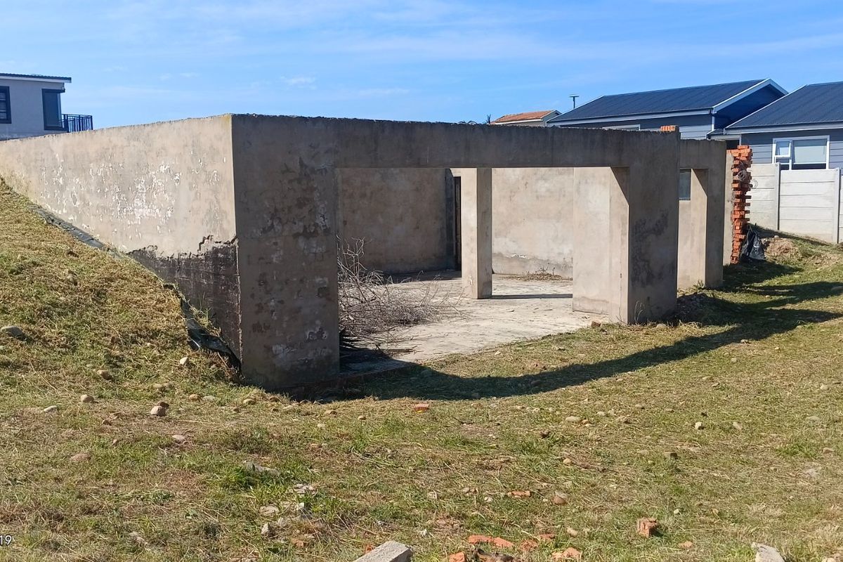 An unfinished concrete structure on a vacant residential plot, featuring a slab foundation and support pillars, requiring completion.