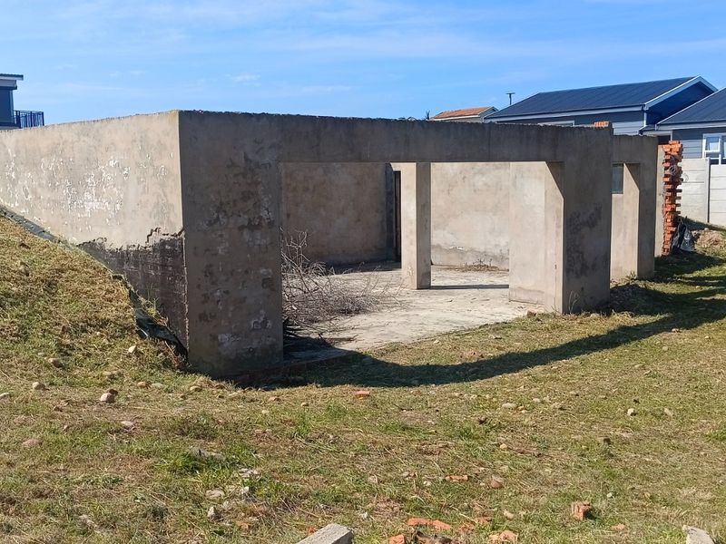 An unfinished concrete structure on a vacant residential plot, featuring a slab foundation and support pillars, requiring completion.