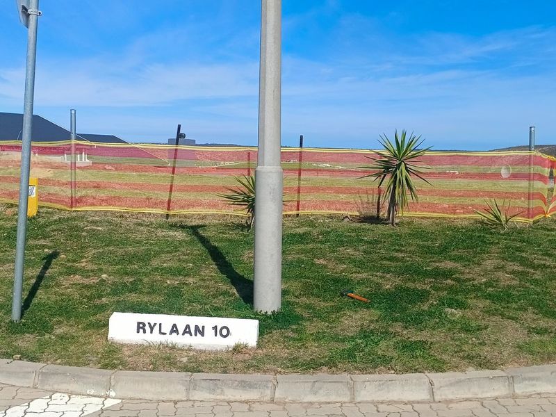 Street view of a vacant residential plot featuring a kerb, pavement, and utility pole, with temporary construction fencing visible on the property boundary.