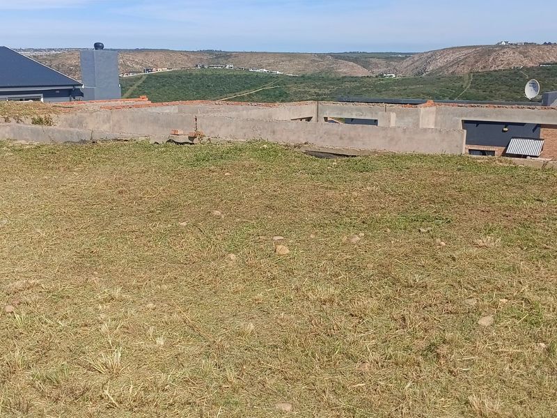 A vacant residential plot featuring an unfinished concrete foundation and brickwork structure, set against a scenic landscape view.
