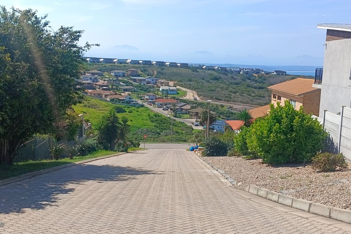 A view looking down a paved residential street towards a coastal landscape and surrounding neighborhood.