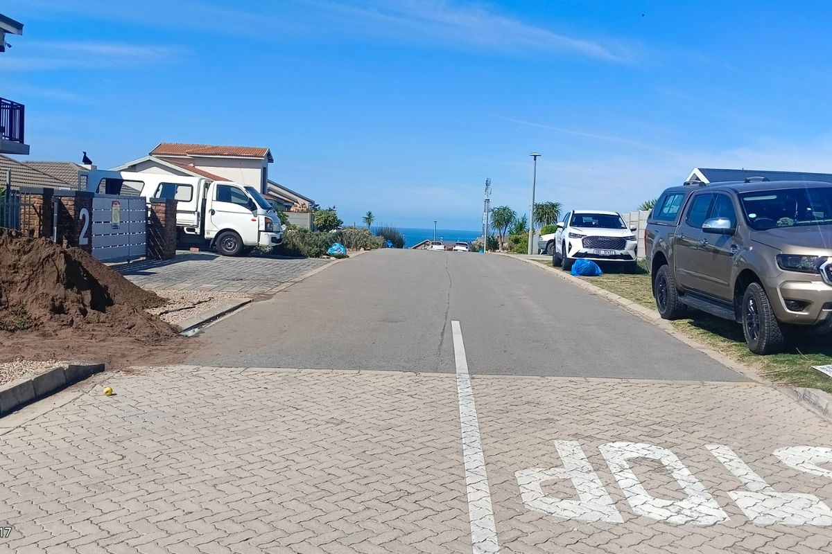 A view of the residential street approach with paved road and sidewalk, leading towards the coastal horizon.