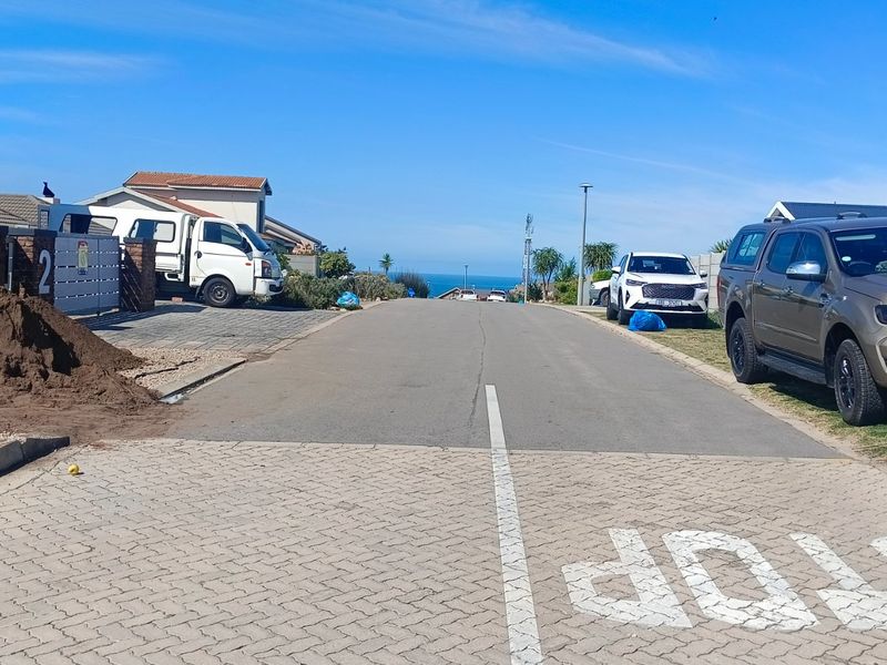 A view of the residential street approach with paved road and sidewalk, leading towards the coastal horizon.