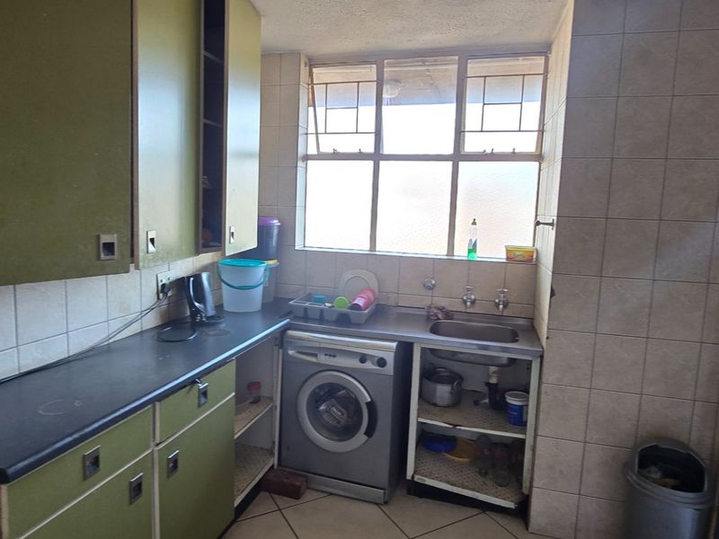 A functional kitchen area featuring built-in cabinetry, a stainless steel sink, and tiled finishes, offering potential for modernization and renovation.