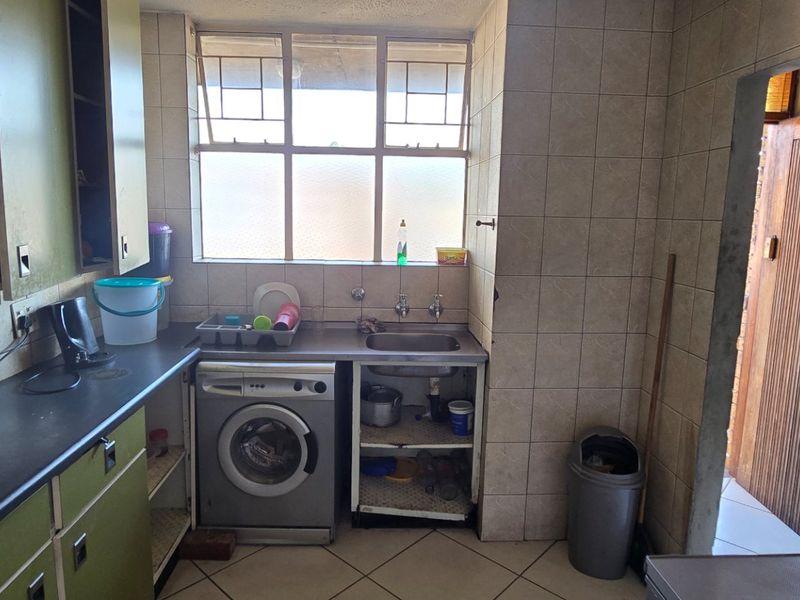 A functional kitchen featuring built-in cabinetry, tiled splashbacks, and a stainless steel sink, offering potential for modernization and aesthetic updates.