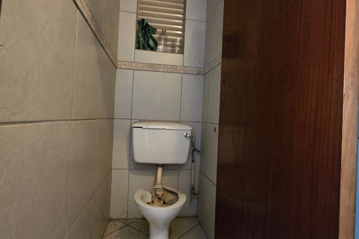 A small bathroom featuring tiled walls and flooring with a recessed niche, currently requiring significant repairs to the toilet fixture.