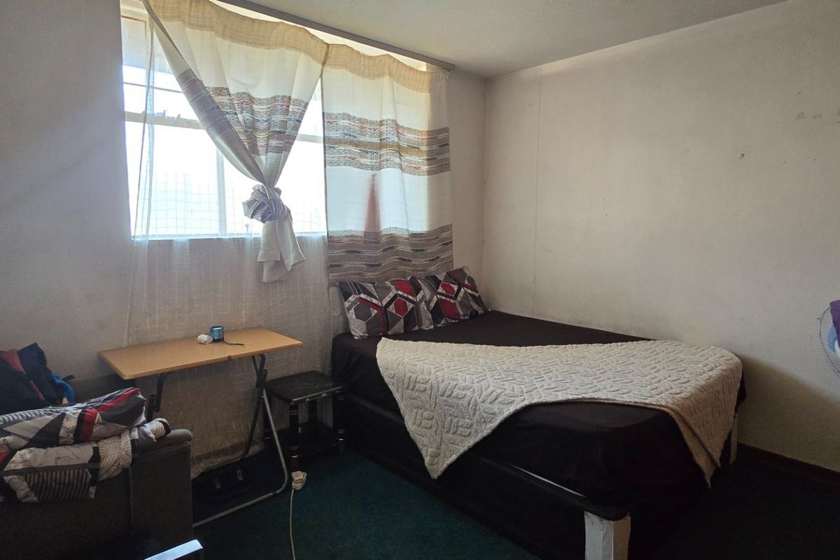 A compact bedroom featuring a window with curtains and standard interior finishes, requiring cosmetic updates to improve its overall condition.