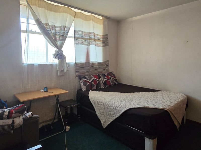 A compact bedroom featuring a window with curtains and standard interior finishes, requiring cosmetic updates to improve its overall condition.