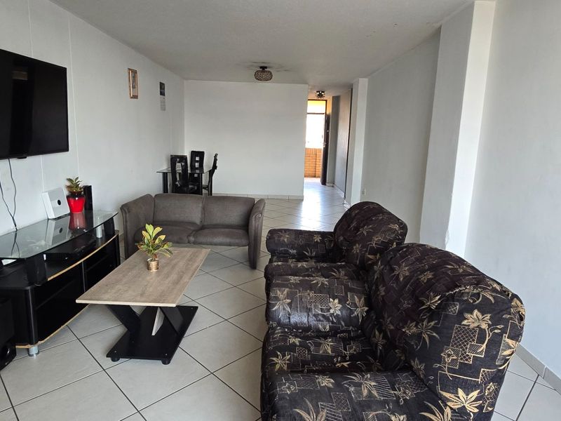 A spacious living room featuring neutral ceramic floor tiles and white walls, offering a functional layout with direct access to the rest of the apartment.