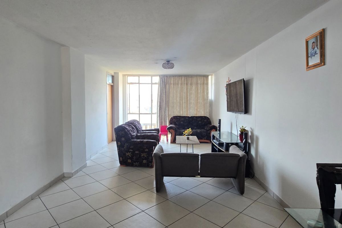 A spacious living room featuring neutral ceramic floor tiles and a large sliding glass door that provides natural light.