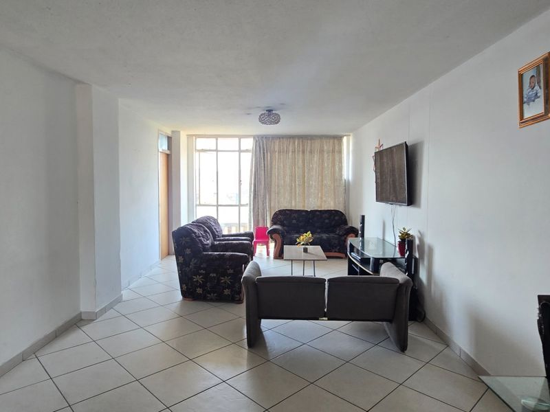 A spacious living room featuring neutral ceramic floor tiles and a large sliding glass door that provides natural light.