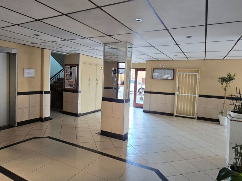 A spacious apartment building entrance lobby featuring tiled flooring, a suspended ceiling, elevator access, and a secure entrance door.