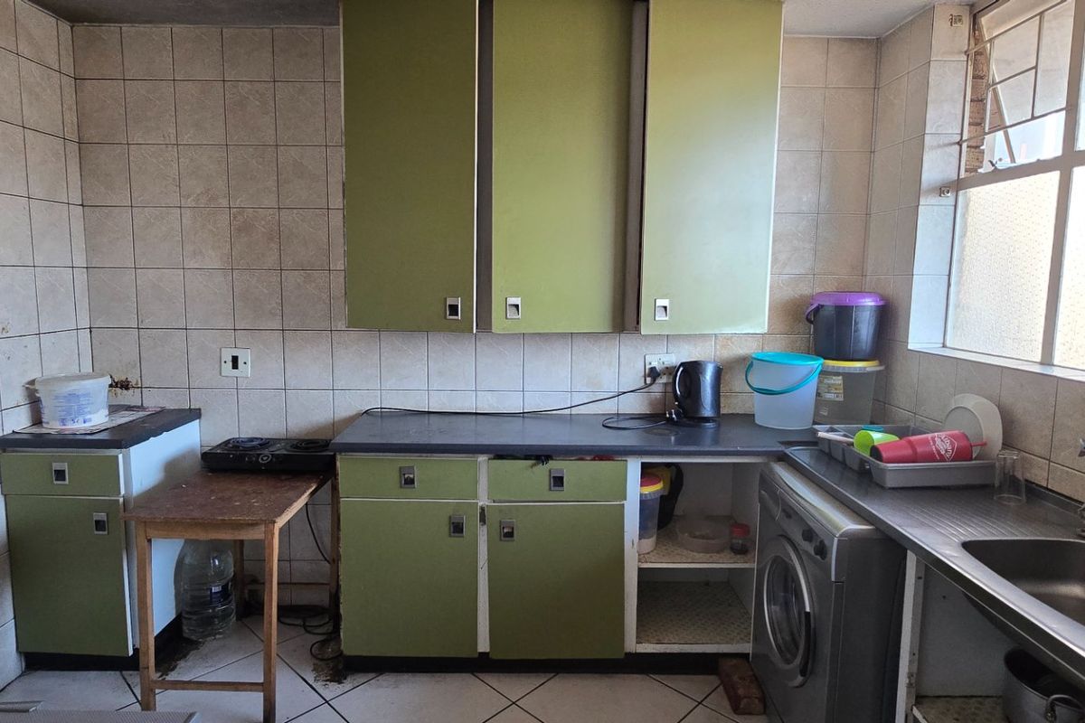 A dated kitchen featuring olive green cabinetry, tiled splashbacks, and a stainless steel sink, offering significant potential for modernization and renovation.