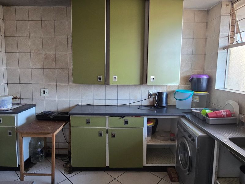 A dated kitchen featuring olive green cabinetry, tiled splashbacks, and a stainless steel sink, offering significant potential for modernization and renovation.