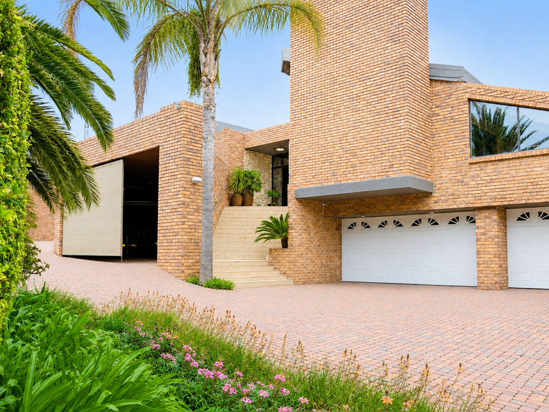 A well-maintained brick-faced residence featuring a paved driveway, double garage, and an elevated entrance accessed by a stone staircase.